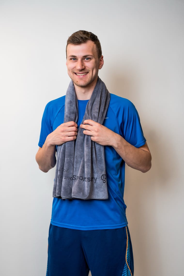 Smilende person med det grå Sportsdry-håndklæde om halsen